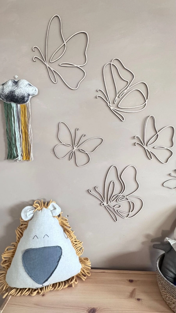 Zestaw 6 drewnianych motylków ze sklejki na ścianie w pokoju dziecka obok lnianych poduszek i dekoracji handmade.