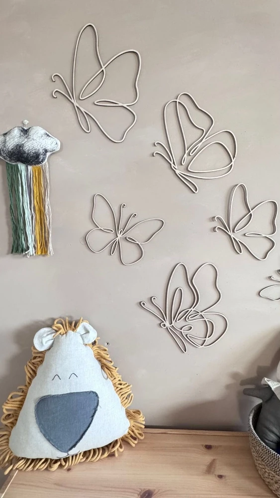Zestaw 6 drewnianych motylków ze sklejki na ścianie w pokoju dziecka obok lnianych poduszek i dekoracji handmade.